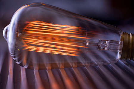 A bright fiery powerful glass incandescent lamp illuminates a dark room around with a fiery orange lightの写真素材