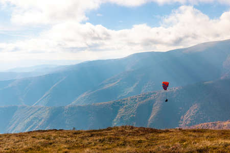 Tourist practices paragliding active sports in highland against giant forestry mountains illuminated by bright sunlight on sunny autumn dayの写真素材