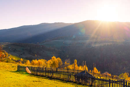 Giant forestry mountains surrounded by heavy fog behind long wooden fence with gate stretching along ground road in highland on autumn dayの写真素材