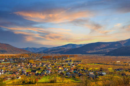 Landscape of village houses scattered in highland valley surrounded by colorful trees under blue sky with low clouds in autumn time-lapseの写真素材