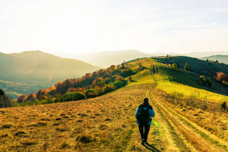 Photographer stands on ground grassy road making photo of autumn landscape with colorful trees and forestry mountains surrounded by fog at sunsetの写真素材