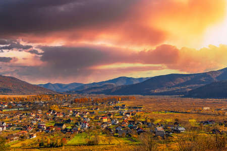 Landscape of village houses scattered in highland valley surrounded by colorful trees under blue sky with low clouds in autumn time-lapseの写真素材