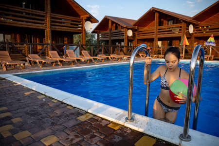 A girl with an inflatable ball in her hands climbs the stairs from the poolの写真素材