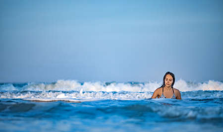 Girl with wet hair in a leopard swimsuit splashes water while sitting in the sea