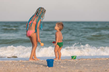 Older sister playing with younger brother aground near the shore on summer vacationの写真素材