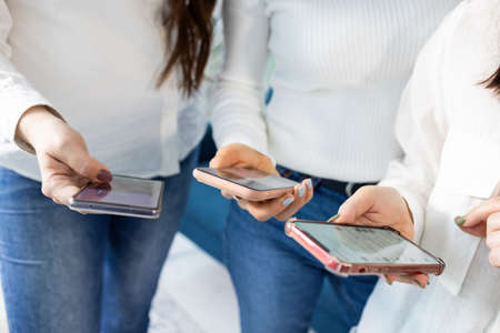 Three modern stylish beautiful smartphones in the hands of interested enthusiastic cheerful girls,...