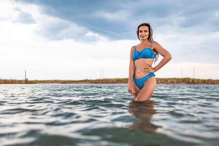 Girl with blond hair in a swimsuit posing against the backdrop of the sunset in the estuary enjoying nature around himの写真素材