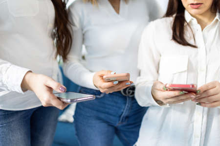 Three smartphones in the hands of girls in shirts and jeans in the studioの写真素材