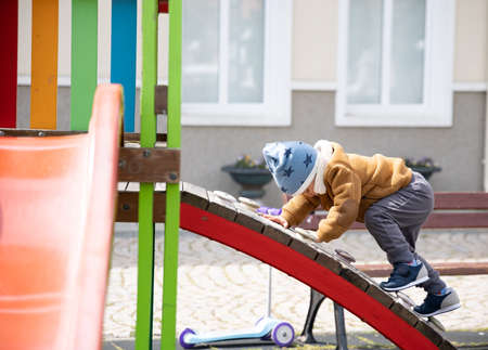A boy on a playground in an autumn park climbs a hill in cloudy weather