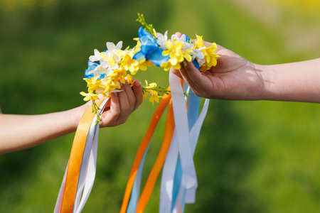 Close-up on Ukrainian wreath with flowers and ribbons in hands of children that brings hope for end of warの写真素材