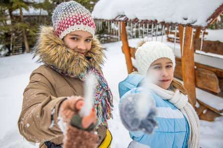 Two girls in winter clothes poke icicles at the camera in the forest