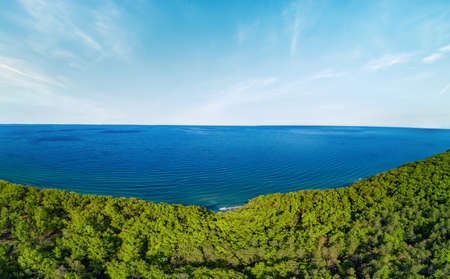 Panorama on small resort village with hotels and inns for summer holidays on rocky wild sharp cliff with green vegetation, above wild calm Black Sea against clear blue skyの写真素材