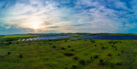 Panorama on modern eco-friendly large solar panels to generate energy from sun's rays are installed in endless meadows with green grass, under blue sky with bright sunの写真素材