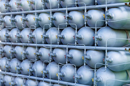 A lot of different small metal bottles filled with gas or gasoline are stacked in large piles and illuminated by the bright warm daytime sunの写真素材