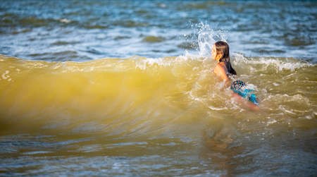 Two lovely tanned long-haired cheerful sisters in bright summer swimsuits cringe and jump in blue...