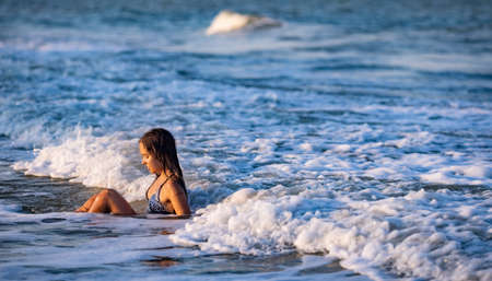 Cheerful wet dark-haired girl with wet hair in a bright leopard bikini swimsuit splashes water...