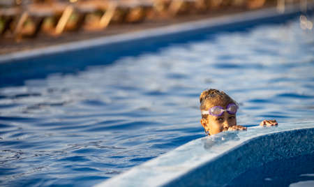 A girl in a bright swimsuit with swimming goggles dives into a pool with clear transparent waterの写真素材