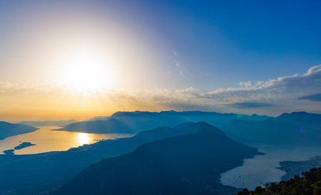 Dazzling sun in the evening sky illuminates all the peaks of the Balkan Montenegrin mountains and the coast of Kotor Bayの写真素材