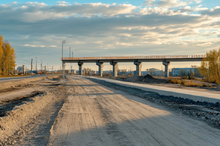 A newly built railway bridge towers over a dusty road as the sun sets, casting warm light across the landscape.の写真素材