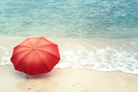 A bright red umbrella stands alone on the warm sandy beach, with gentle waves lapping at the shore.の写真素材