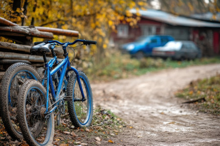 Two blue bicycles lean against a wooden fence along a dirt path lined with colorful autumn leaves.の写真素材