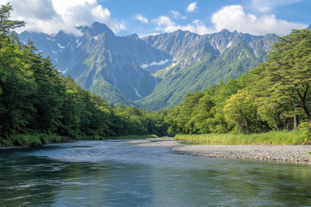 A clear river gently winds through a verdant valley, framed by towering mountains under a bright blue sky.の写真素材