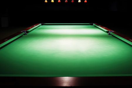 A well-lit green pool table awaits players in a dimly lit room, with colorful balls suspended above.の写真素材