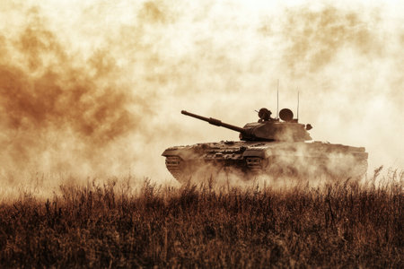 A tank maneuvering through a field, surrounded by clouds of dust and smoke during a golden hour.の写真素材