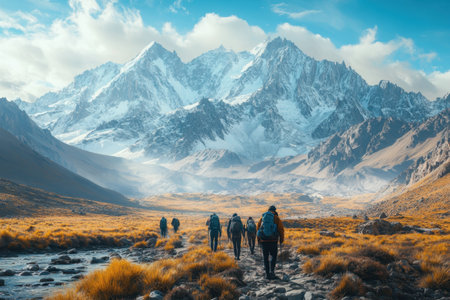 Groups of hikers navigate a scenic mountain valley adorned with autumn grasses and dramatic peaks.の写真素材