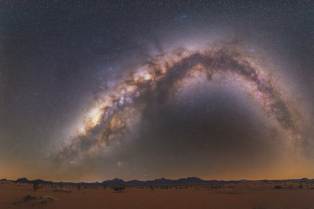 A breathtaking display of the Milky Way stretches across the night sky above an arid desert, highlighting stars.の写真素材