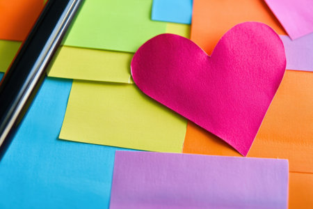 Brightly colored sticky notes surround a pink heart cutout with a black pen resting nearby, creating a cheerful look.の写真素材