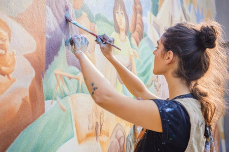 A dedicated artist applies bright colors to a large mural, showing creativity on a city wall during daytime.の写真素材
