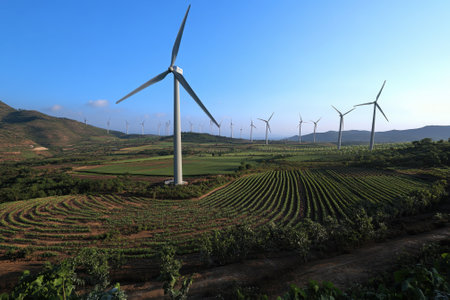 Wind turbines stand tall over a lush green landscape, symbolizing renewable energy generation in farming areas.の写真素材