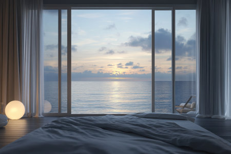 The room features a large window overlooking calm ocean waves as the sun sets on the horizon.の写真素材