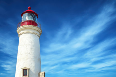 Historic lighthouse rises against a clear blue sky, symbolizing coastal navigation and safety near the shore.の写真素材