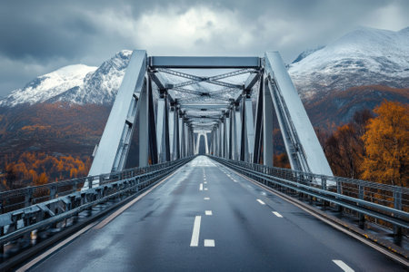 Modern bridge stretches over a smooth road with mountains and colorful autumn trees in the background.の写真素材