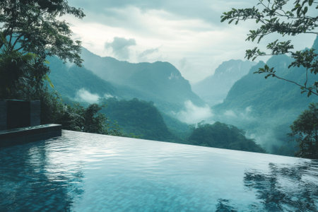 A serene infinity pool offers breathtaking views of misty mountains and lush valleys in a tranquil setting.の写真素材