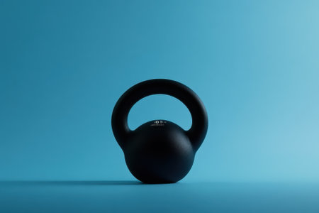 A black kettlebell sits on a flat surface, contrasting sharply with a vibrant blue background.の写真素材