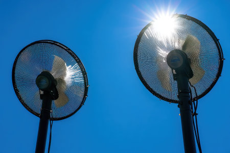 Two large industrial fans stand tall against a bright blue sky, offering a refreshing breeze on a sunny day.の写真素材