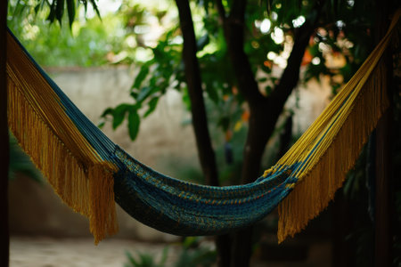 A vibrant hammock slopes between trees, inviting relaxation under the sun in a tranquil garden.の写真素材
