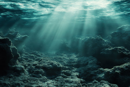 Sunlight filters through water, highlighting rocky seabed and coral formations under the ocean surface.の写真素材