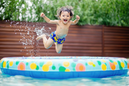 A young child is having fun, leaping into a vibrant inflatable pool, surrounded by greenery and sunshine.の写真素材