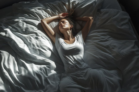 A woman lies in a sunlit bedroom, surrounded by white sheets, exuding tranquility and relaxation.の写真素材