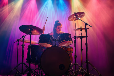 A skilled drummer passionately plays on stage, illuminated by vibrant colored lights during a live music performance.の写真素材