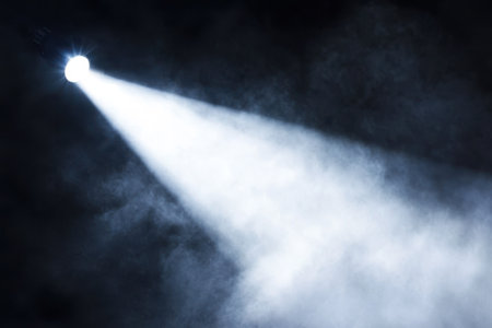 A strong spotlight shines through a dense fog, creating a dramatic atmosphere suitable for a performance.の写真素材