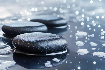 Smooth black stones rest peacefully in calm water, reflecting soft light and surrounded by delicate ripples.の写真素材