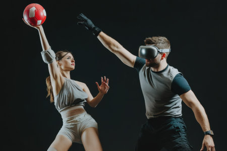 A male wearing virtual reality goggles defends against a ball thrown by a female athlete in motion.の写真素材