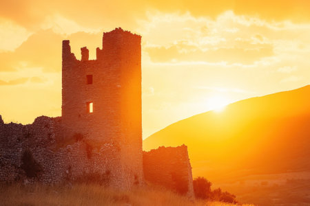 A weathered tower stands tall in the foreground as a sunset casts golden hues over the hills.の写真素材