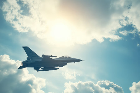 A military jet maneuvers through the sky, surrounded by fluffy clouds and illuminated by sunlight.の写真素材