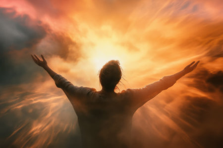 A figure stands with outstretched arms, welcoming the stunning hues of a sunset in the sky, radiating warmth.の写真素材